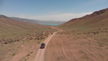 Yukarıdan gelen kamera dağlardan geçen iki off-road aracını takip ederek güzel bir dağ gölüne doğru gidiyor..