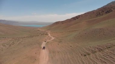 İki turist cipi dağların arasında çok güzel bir geçitten geçiyor. Güzel bir dağ gölü manzarası. Üretici off-road yolu.