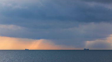 Bulutlu havada ufukta iki gemi var.