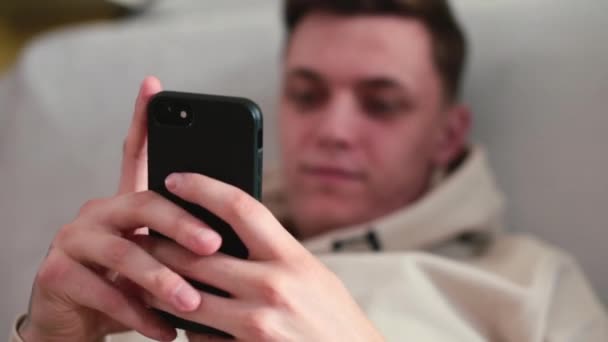 Ein junger Mann hält ein schwarzes Telefon in der Hand. Drückt seine Finger auf den Bildschirm. — Stockvideo