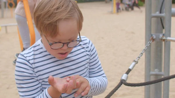 Síndrome de Down chico trata en mano de escarabajo. Él mira de cerca, examina el objeto. —  Fotos de Stock
