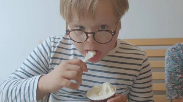 O rapaz da síndrome de Down come gelado com uma colher. Desfrute de sobremesa fria. — Fotografia de Stock