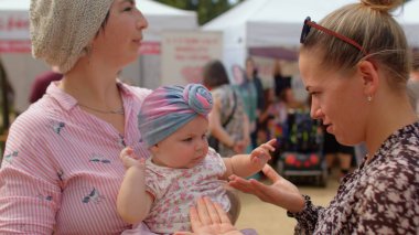 Halka açık bir yerde mutlu bir çocuğu olan iki genç kadın, anneye yakın bir bebek..