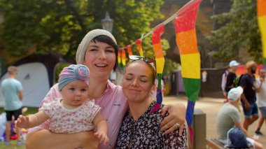 Çocuklu mutlu LGBT çifti gökkuşağı bayraklarının yanında yürüyor. Bebekli aile.