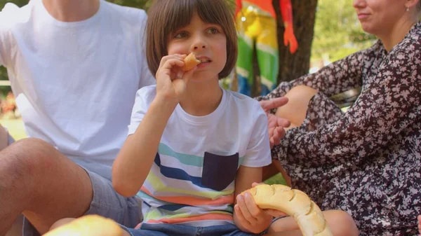 A boy eats a baguette during a family picnic. Summer is for eating outdoors. — Stock Photo, Image