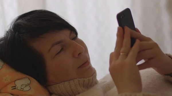 Kadın cep telefonlu elleri kullanıyor. Yatakta yatıyor. Boş zaman evde dikkat ekran aleti. — Stok fotoğraf
