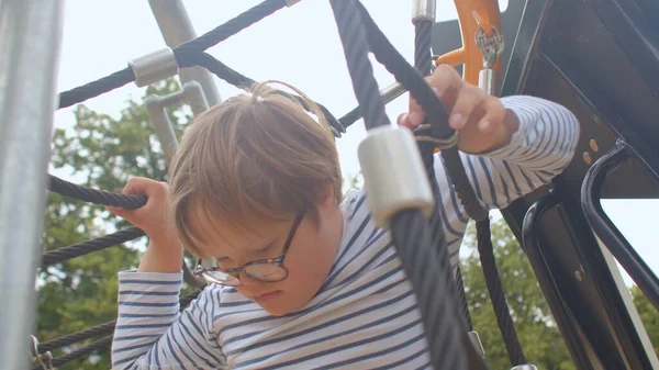 Junge mit Down-Syndrom zwingt sich an den Seilen des Spielplatzes entlang. — Stockfoto