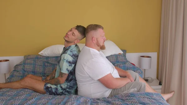 Deux gars s'assoient dos à dos sur le lit dans la chambre. Ils parlent, prennent place — Photo