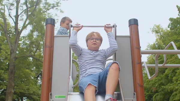 Down syndrome boy rides on playground slide. A bright moment of childhood joy. — Stock Photo, Image