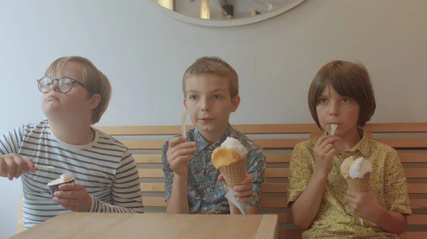 10代の3人がカフェでアイスクリームを食べています。手を振って男の子ダウン症候群. — ストック写真