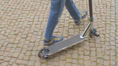 Bir genç, kaldırımda scooter kullanıyor. Ata bindikten sonra çelik