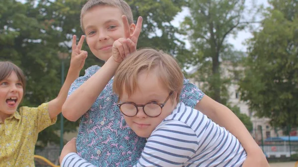 En tonåring hjälper en pojke med nedsatt syndromet att sätta på glasögon Nära relationer. — Stockfoto
