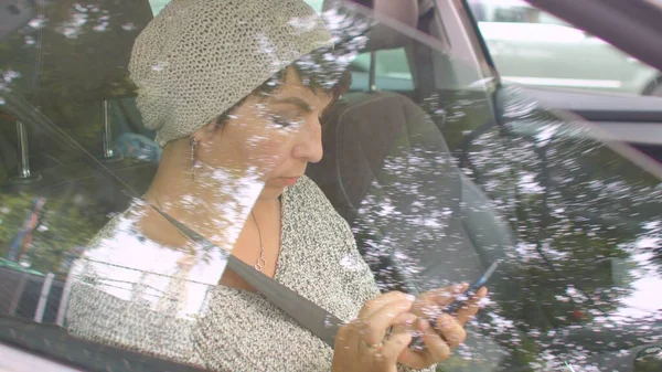 Žena používá v autě telefon. Střelba skrz sklo, odraz světlice. — Stock fotografie
