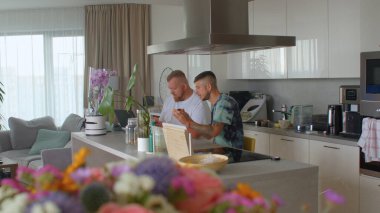 İki adam apartman dairesinde kahvaltı yapıyor. Masaya otururlar, yemek yerler..