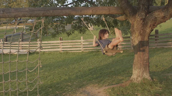 Chico monta columpio de árbol en el pueblo. Pasar tiempo libre solo de vacaciones. —  Fotos de Stock