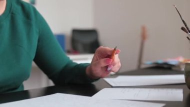 Kalemi eliyle tutuyor, çeviriyor. Odaklanma sırasında hareket eden kadın.
