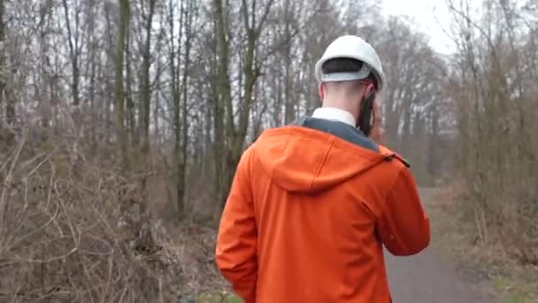 De achterkant van een arbeider in een helm, hij praat aan de telefoon — Stockvideo