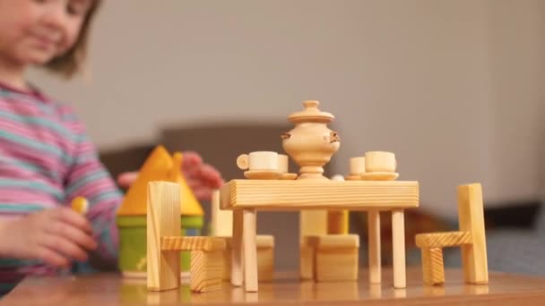 那女孩用手触摸着一个木制玩具.有茶具的桌子. — 图库视频影像