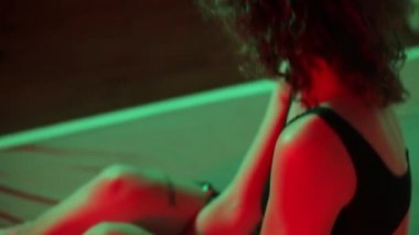 Kadın çılgınca gülüyor, kırmızı ışık partisi veriyor, yatağa düşüyor, yüzünü ellerle örtüyor.