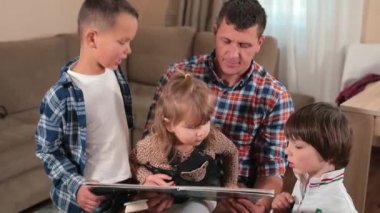 Müstakbel baba evdeki çocuklara kitap okuyor. Eller sayfaları gösteriyor..