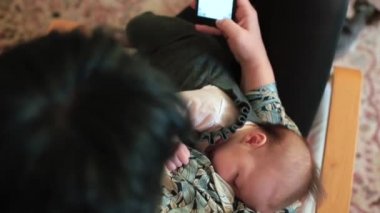 Yeni doğmuş bebeği ve telefonu olan bir kadın. Çocuk doktoruyla çevrimiçi yazışmalar.