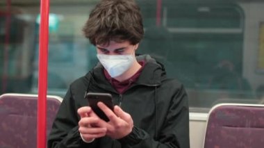 Maskeli adam metroda telefon kullanıyor. Kulağına fındık koyup mesajı dinliyor..