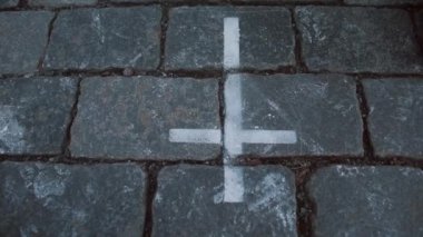 Bir adamın eli, bir taşın üzerinde beyaz bir haçın üzerine konur..