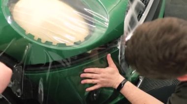 Tamircilerin elleri araba modülünün boyasında koruyucu vinil katmanı tutuyor..