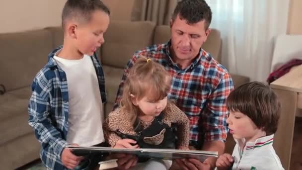 活跃的父亲在家里给孩子们读一本书。手指向书页. — 图库视频影像