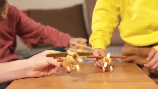 A gyerekkezek fa repülőgépekkel játszanak az asztalon. A felszállást szimulálják.. — Stock videók