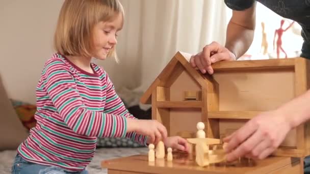 Una chica juega con un profesor en una casa de madera. Ella pone figuras con sus manos. — Vídeo de stock