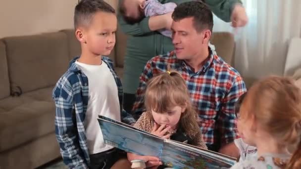 Large family reads book home father holds daughter in arms, next to his sons. — Stock Video