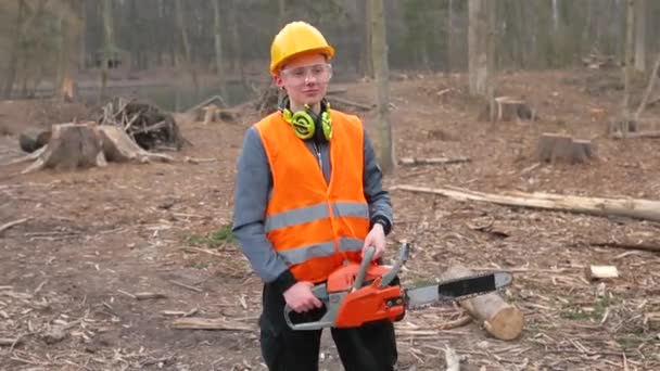 Lány munkaruhában, láncfűrésszel a kezében, pózol a fakitermelési területen.. — Stock videók