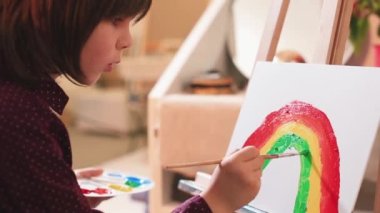 Öğrenci tuvale gökkuşağı resmi çiziyor. Kendini izole ediyor. Yeşil boyayı fırçayla boyuyor.