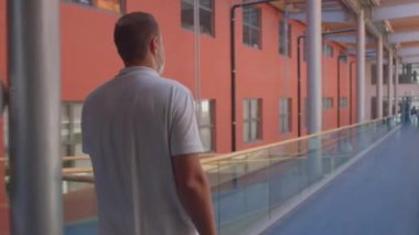 Arkadaki adam büyük bir odada koridor boyunca ilerliyor..