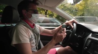 Maskeli adam araba sürerken telefon kullanır. Mesaja cevap veriyor..