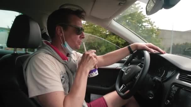 L'homme boit de la limonade en conduisant une voiture. Il suce avec un tube.. — Video