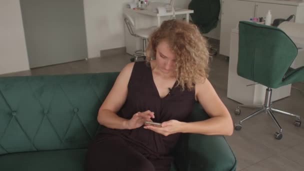 Het meisje gebruikt de telefoon op de bank. Ze drukt op haar vingers op het scherm.. — Stockvideo