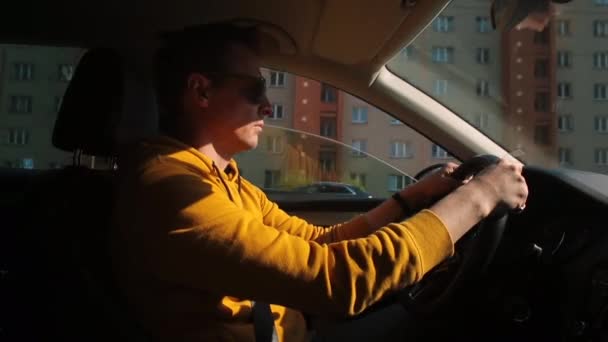 Man drives a car in the sun city He holds steering wheel hands, controls road — Stock Video