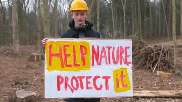 Un joven sostiene un cartel que ayuda a la naturaleza a protegerla, en el bosque. — Vídeo de stock