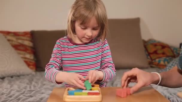 Het meisje verzamelt een puzzel op tafel. De leerkrachten hand helpt in het bedrijfsleven. — Stockvideo
