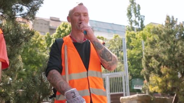An employee in an orange vest smokes a vape. He releases steam into the light. — Stock Video