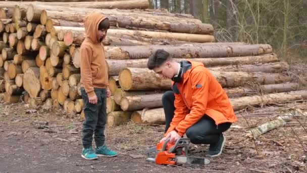 Młody menedżer uczy dziecko korzystać ze szkoły leśnictwa piłą łańcuchową w wyrębie. — Wideo stockowe