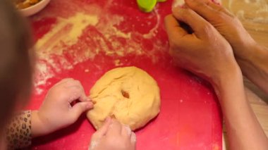 Anne ve kızının elleri kırmızı tahtada hamuru yoğuruyor..