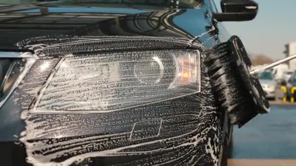 Szczotka do mydła pociera reflektor samochodu w myjni samochodowej. — Wideo stockowe