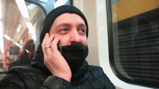 Homem mascarado fala ao telefone no carro do metro. Ele segura gadget sua orelha. — Vídeo de Stock