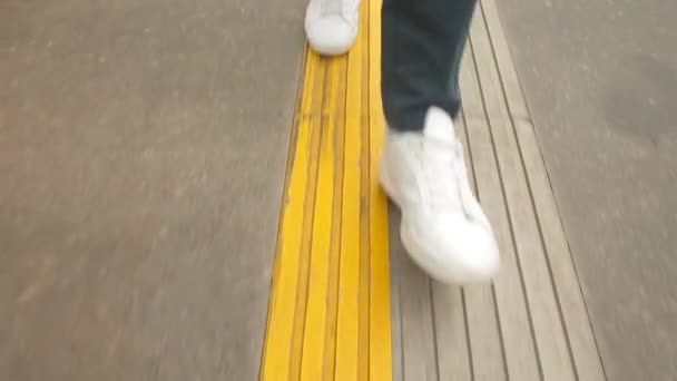 Τα πόδια λευκά sneakers κάνουν βήματα στην κίτρινη γραμμή. Συνοριακός σταθμός ασφαλείας — Αρχείο Βίντεο