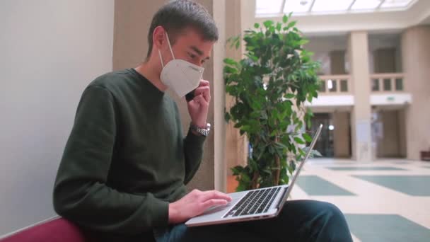 仮面の男はインターネットを使ったノートパソコンと電話のホテルロビーのフリーランスの仕事を使う — ストック動画