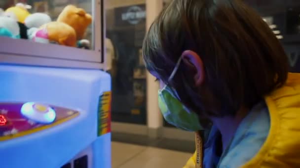 Criança na máscara lança moeda na máquina de fenda com brinquedos, comece o jogo do acaso — Vídeo de Stock