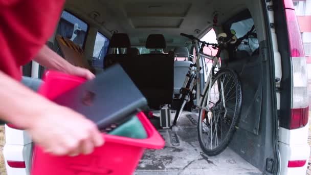 Уставший человек в защитной маске загружает коробку с личными вещами в машину. — стоковое видео